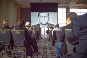 Photo by Aaron Warnick | Photo Editor. The crowd in the Power Center Ballroom on Friday watches a clip of Oliver Stone’s new series at a symposium dedicated to the study of the Kennedy assassination. The three-day conference brought together experts to discuss their research. 