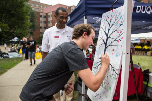Photo by Claire Murray | Photo Editor. Student Government Asssociation President John Foster (back) watches as incoming freshman Chris Collins (front) signs his name on a piece of art at an orientation event Tuesday on Assumption Commons. Duquesne’s highly-regarded orientation program took on a new theme this year called “This World, Our Path, My Mark.”